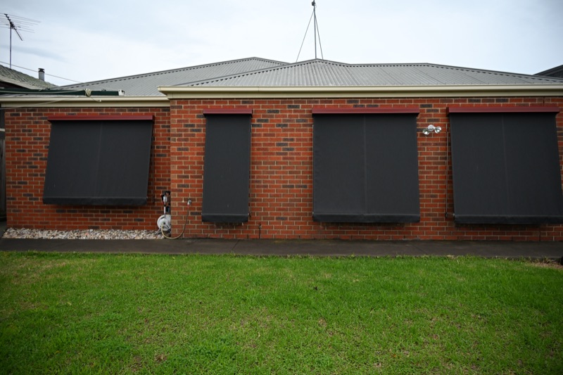 Four charcoal auto spring awnings fully extended across the exterior windows of a red brick home
