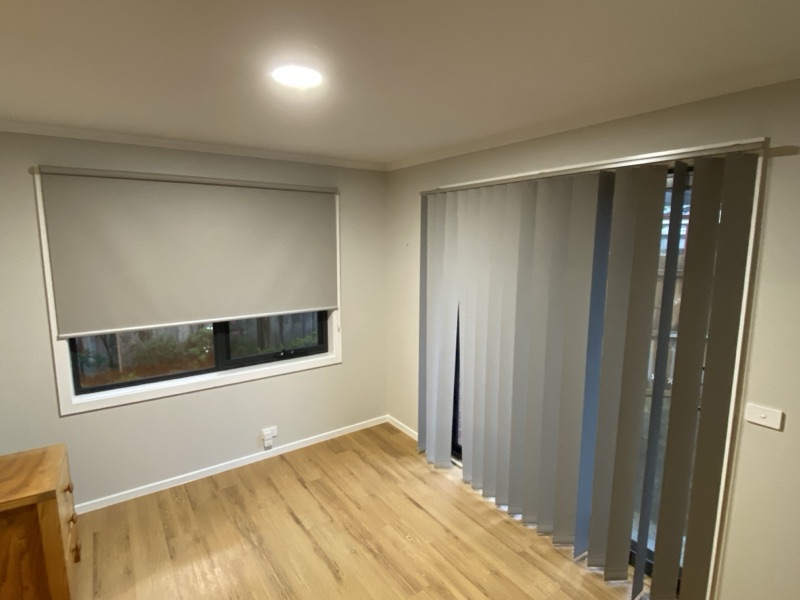 Room showing a grey roller blind on a window and grey vertical blinds on a sliding door before installation of new window furnishings