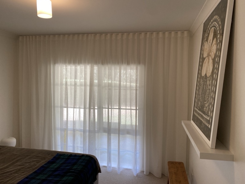 White wave-fold sheer curtains covering a full-height sliding door in a bedroom, allowing soft diffused light while maintaining privacy