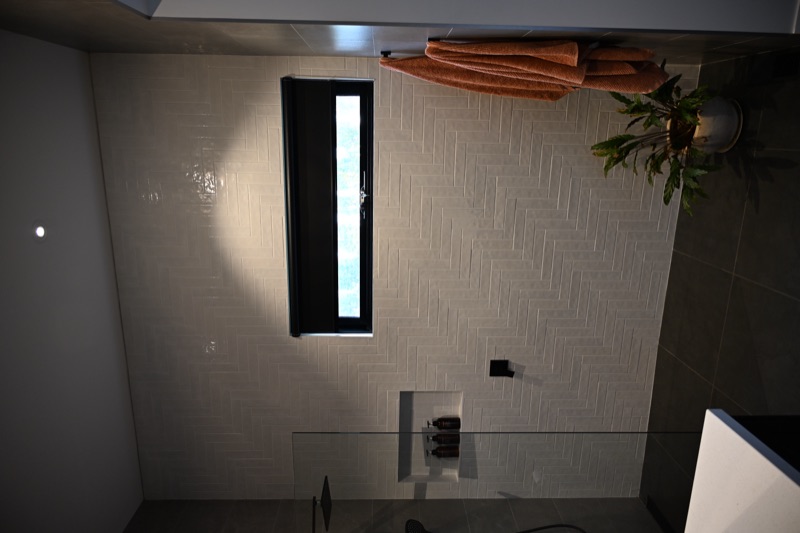 Black roller blind installed in a herringbone-tiled ensuite bathroom window, providing privacy beside the shower